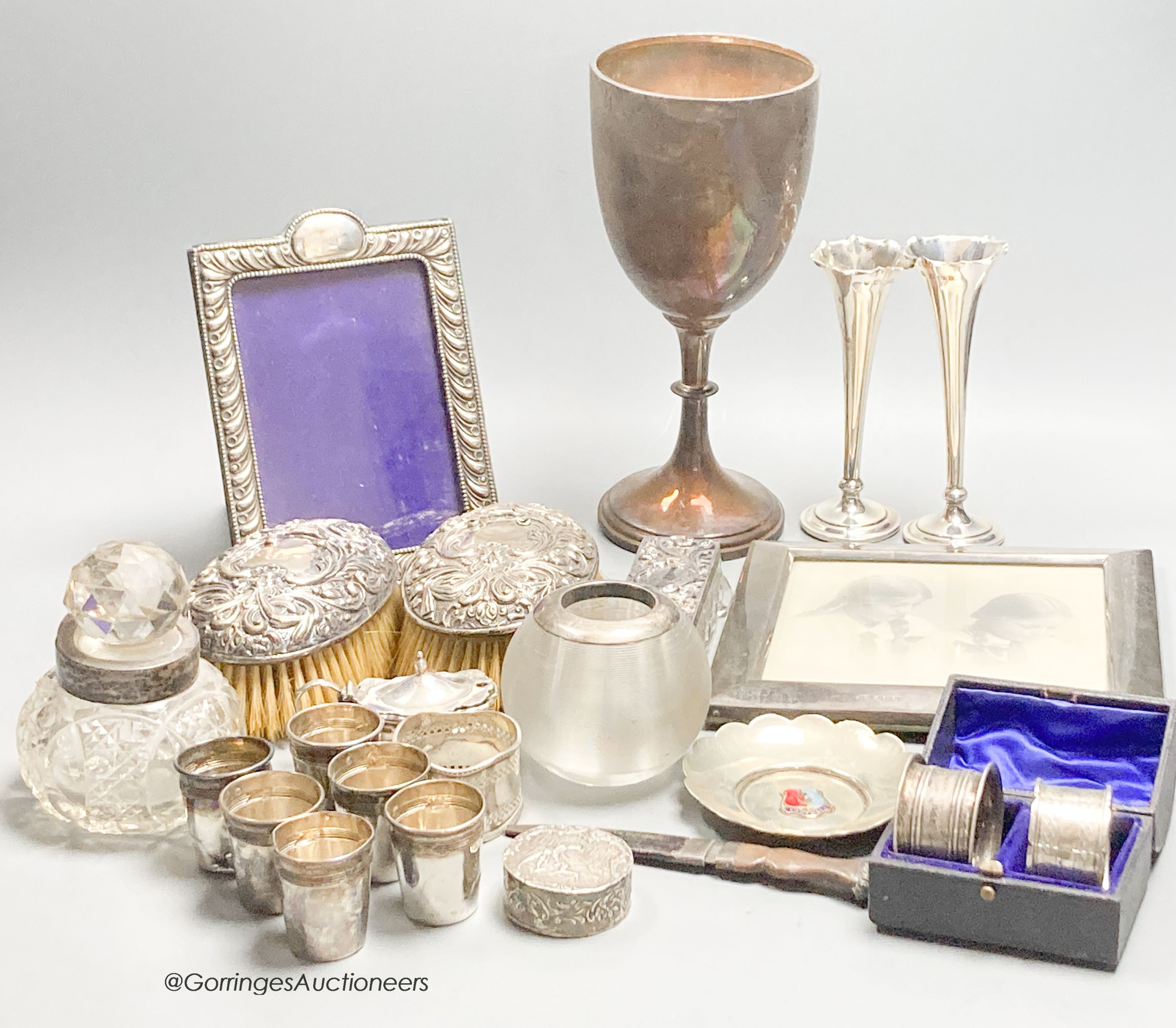 Sundry small silver including a trophy goblet, 22.5cm, napkin rings, two photograph frames, match tidy, spill vases, brushes, white metal tots and box etc.